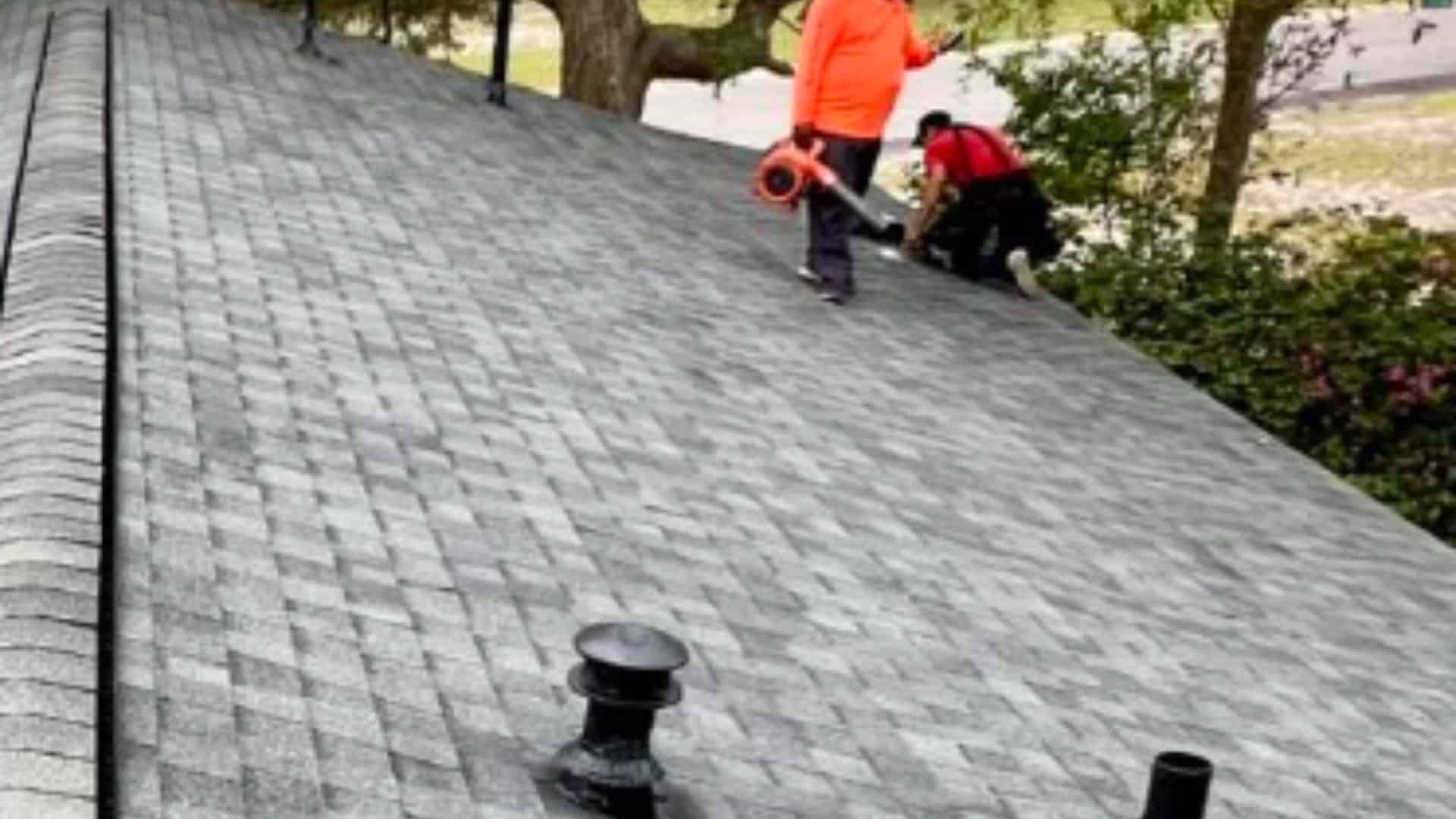 Can an existing roof be fortified? Roofing professionals working on a roof with gray shingles, one person using a blower while the other inspects the roof's condition to see if it can be Fortified.