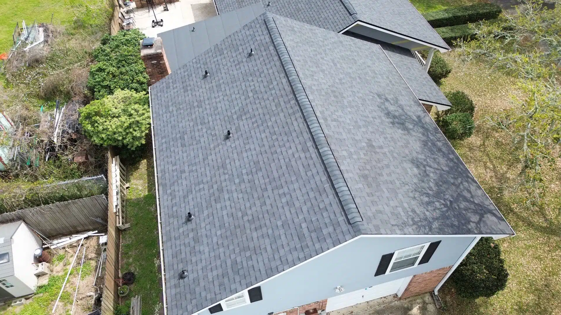 Drone image of a complex residential roof structure with multiple gables and chimneys, surrounded by a landscaped yard and neighboring homes.