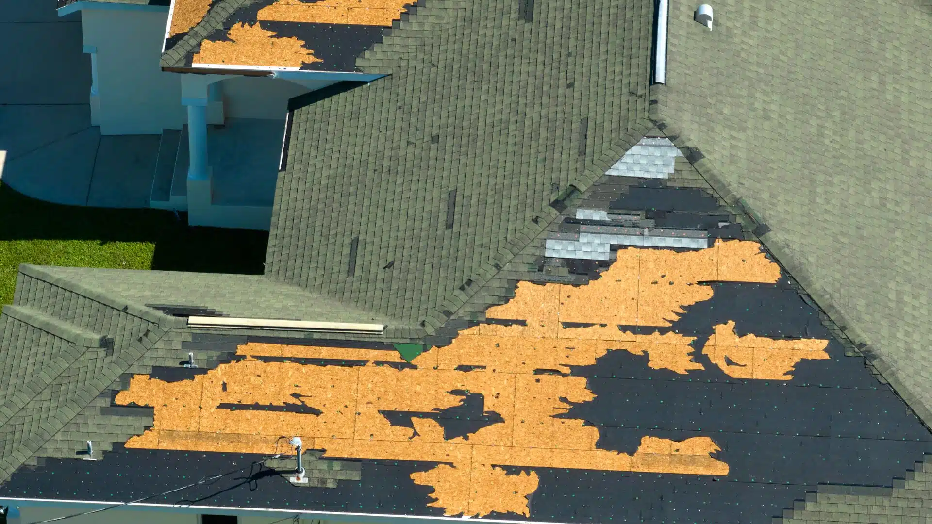 Shingles ripped from roof after hurricane, exposing plywood decking—an urgent call to contact a roofer near me for fortified roofing solutions with hurricane-resistant materials