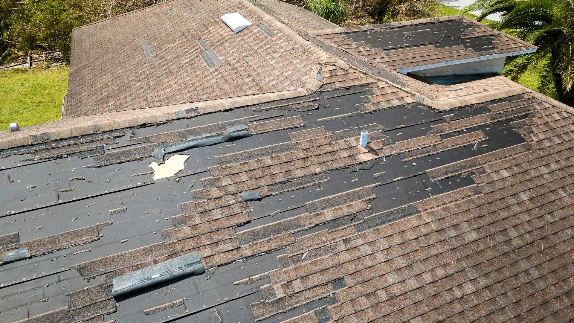 A close-up view of a roof severely damaged by high winds and storm debris, showcasing torn shingles and exposed underlayment, highlighting the impact of a hurricane on residential roofing in Gulfport MS.