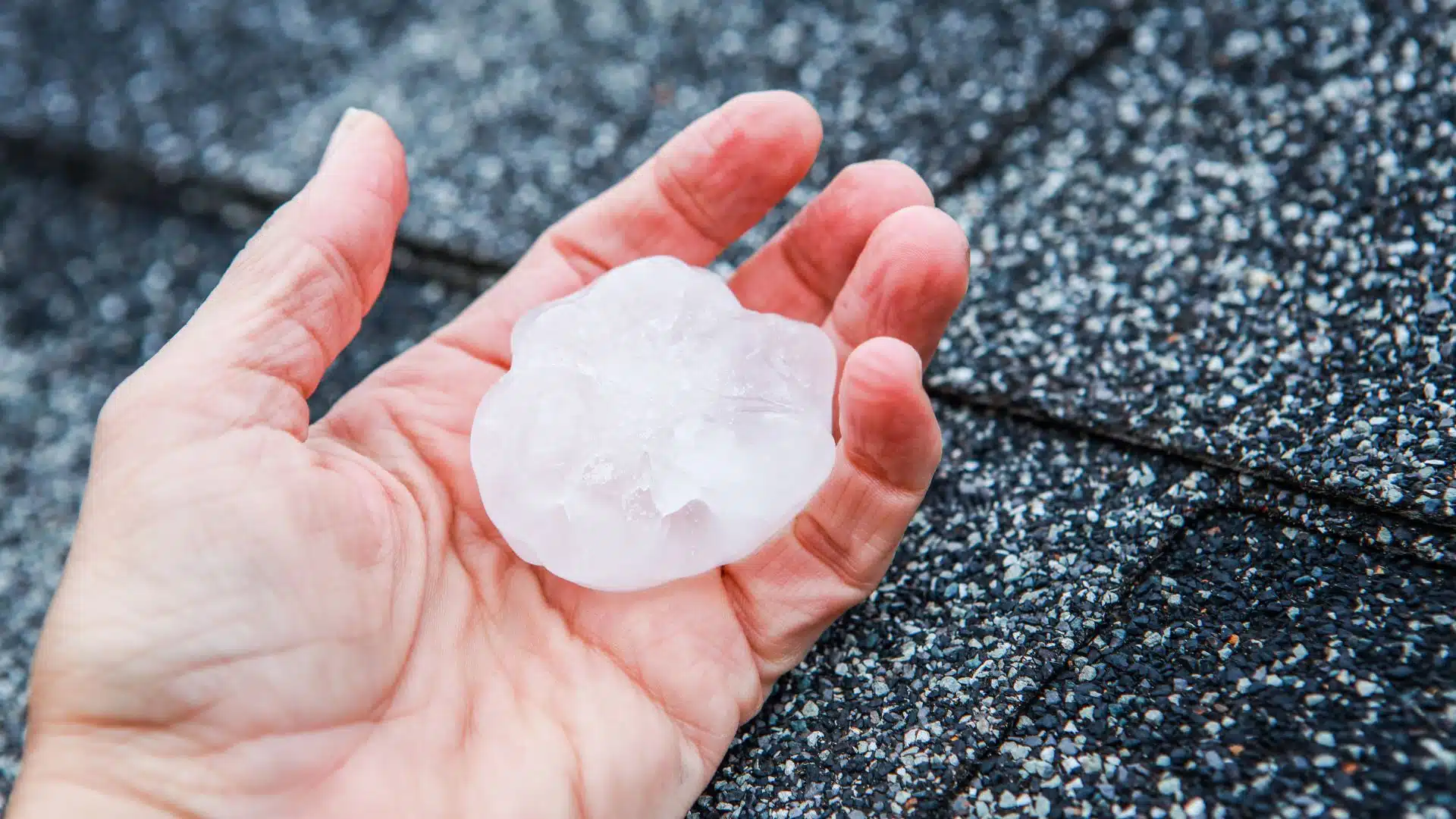 Hand holding large hailstone on a roof surface, demonstrating the potential damage hail can cause during a hurricane.