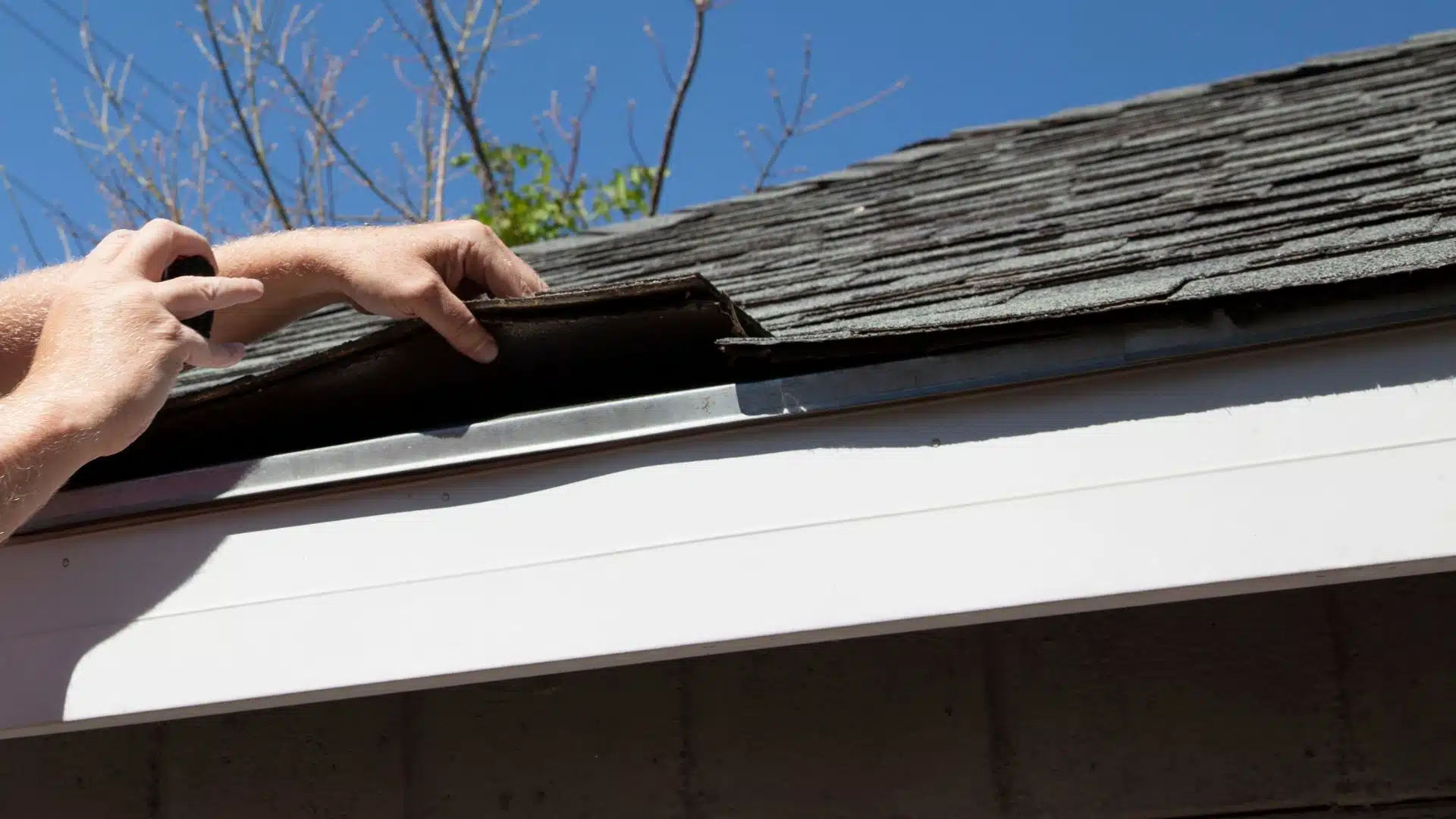 Roofing contractor in Gulfport, MS lifting shingles during a roof inspection to check for storm-related vulnerabilities before hurricane season.