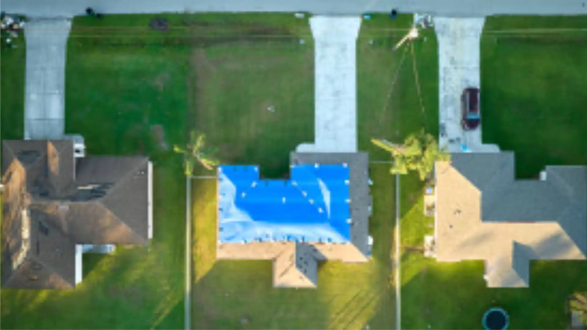 Aerial view of Gulfport MS homes with blue tarps on storm-damaged roofs, illustrating the local roofing challenges coastal homeowners face after hurricanes.
