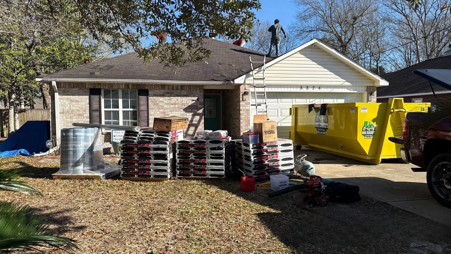 Roof replacement in progress in Gulfport MS with shingles, dumpster, and crew preparing a home for hurricane-ready roofing system